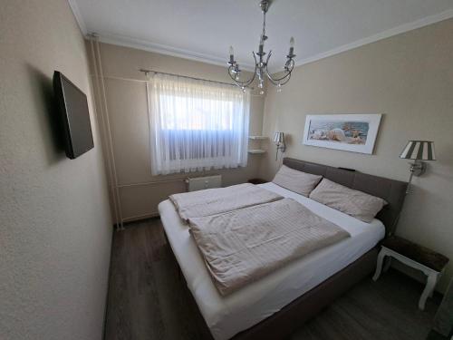 a bedroom with a bed with white sheets and a chandelier at App 17 Haus Nordland in Sylt