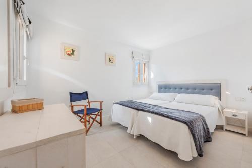 a white bedroom with a bed and a chair at Ull de Bou in Port de Pollensa