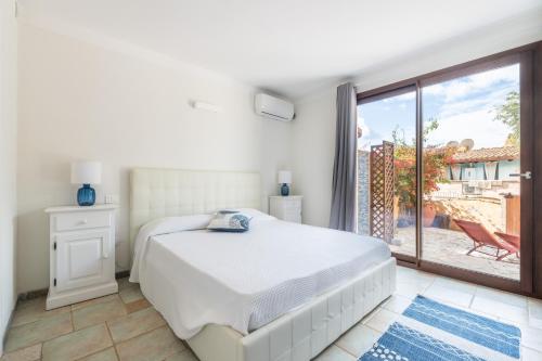 a white bedroom with a bed and a large window at L'Angolo di Noemi - Chia in Chia