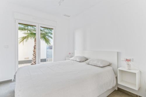 a white bedroom with a white bed and a palm tree at El Sueño in Orihuela