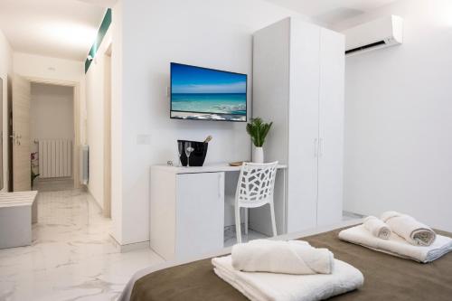 a white bedroom with a desk and a tv on the wall at Fantasia House in Marsala