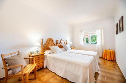 a white bedroom with a bed and a chair at Villa Can Andreuet de Baix in Illes Balears