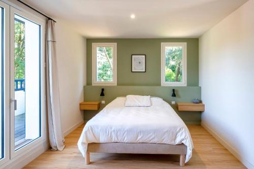 a bedroom with a bed and two windows at Villa proche du lac d'Hossegor in Soorts-Hossegor