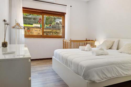 a white bedroom with two beds and a window at Vermarl - Viana do Castelo in Linhares de Cima