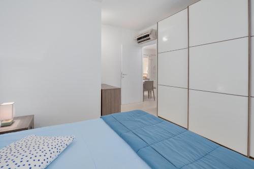 a white bedroom with a blue bed and a mirror at Cormorani - Appartamento 3 in Golfo Aranci