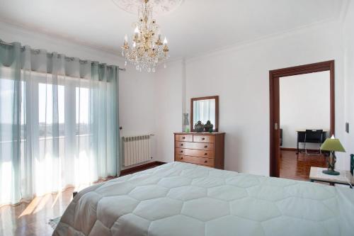 a white bedroom with a large bed and a chandelier at Casa Imaginário Com Serenidade in Caldas da Rainha