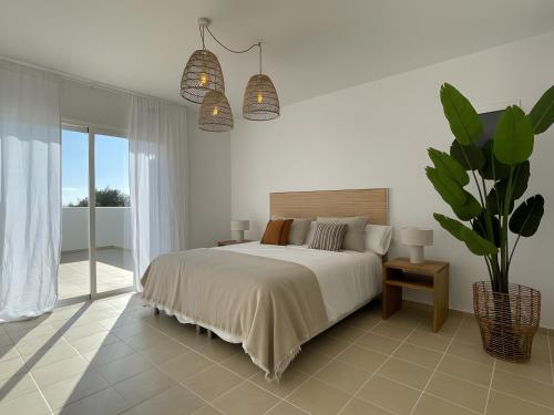 a white bedroom with a bed and a potted plant at Casa da Lúa in Sant Lluis