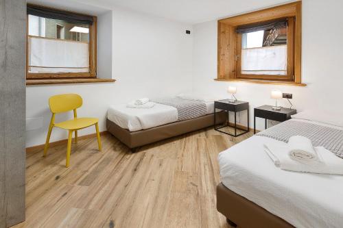 a bedroom with two beds and a yellow chair at Appartamento Via Livigno in Isolaccia