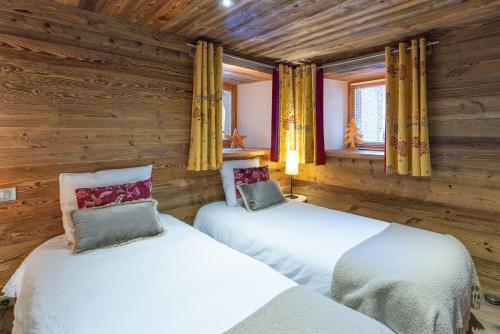 two beds in a room with wooden walls and windows at Coeur de neige 1724 in Le Grand-Bornand