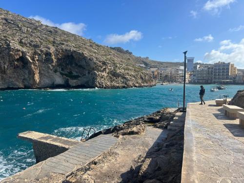 a person standing on a walkway next to the ocean at Arzella Apartments Xlendi, Premium 2BR, Bus Stop & Market Opposite in Xlendi