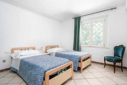 two beds in a room with a chair and a window at La vela gialla in Cala Liberotto