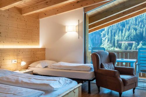 a bedroom with two beds and a chair and a window at Hotel Residence Gardena Dolomites in Santa Cristina Gherdëina