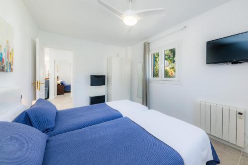 a white bedroom with a blue bed and a tv at Apartamento La Pergola in Font de Sa Cala
