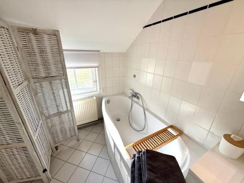 a white bathroom with a tub and a window at Lüttje Reethuus in Südbrookmerland