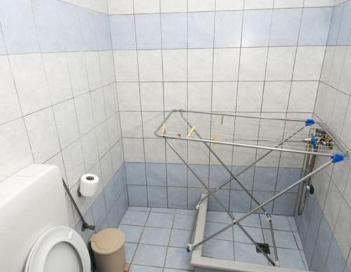 a white tiled bathroom with a toilet and a shelf at Dimitrakis Studios in Masouri