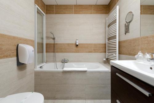 a bathroom with a tub and a toilet and a sink at Hotel Garzon Plaza in Győr