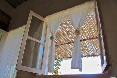 a window with white curtains and a straw roof at FARINHA DE PAU - ECO B&B in Tarrafal