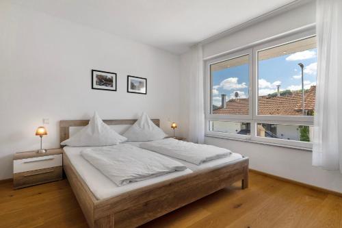 a white bedroom with a bed and a large window at Ferienwohnung Rebenrain, 80qm in Steinach