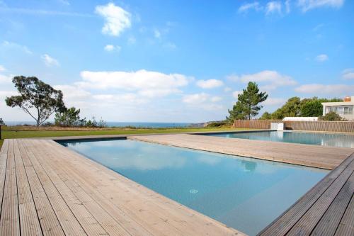 a swimming pool with a wooden deck and the ocean at Luxury Boho Style Apartment Nazaré in Nazaré