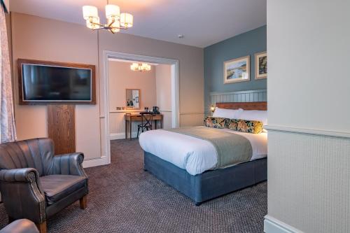 a bedroom with a bed and a chair and a television at The Swan Inn by Innkeeper's Collection in Horning
