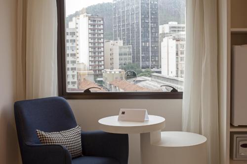 a room with a blue chair and a table and a window at ibis Styles Rio de Janeiro Botafogo in Rio de Janeiro