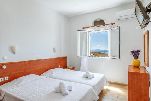 two beds in a white room with a window at Anemologio 102 Tinos in Agios Ioannis