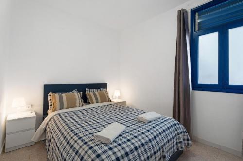 a bedroom with a bed with a checked blanket and a window at Apartamentos Playa Azul - 8 in Vallehermoso