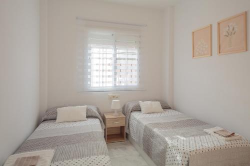 two beds in a white room with a window at El Rincón Sevillano in Gerena