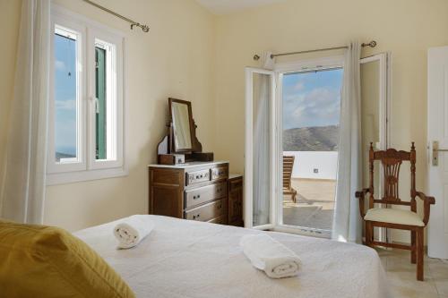 a bedroom with a bed and a window and a chair at Aegean Villas Ios in Ios Chora