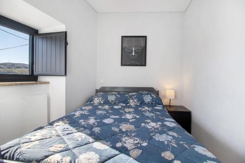 ein Schlafzimmer mit einem Bett mit blauer Bettdecke und einem Fenster in der Unterkunft Casaesquerda Cinza in Vieira do Minho