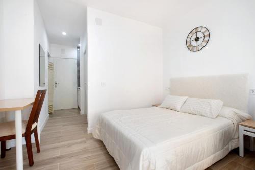 a white bedroom with a bed and a desk and a clock at Apartamento Los Manantiales in Torremolinos