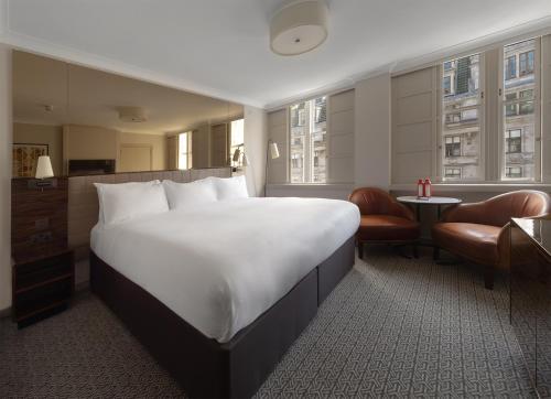 a hotel room with a large white bed and chairs at Strand Palace in London