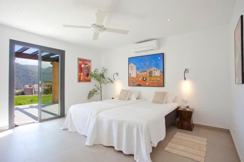 a white bedroom with a bed and a large window at Villa Mar y Muntana in Banyalbufar