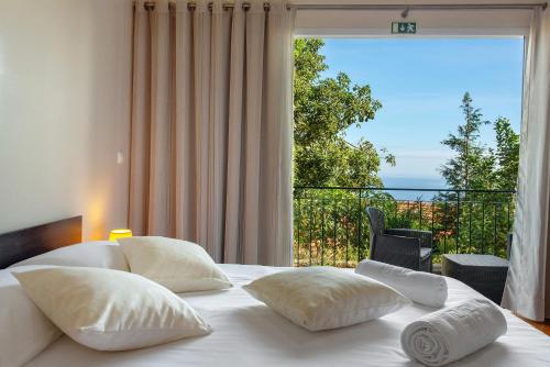 a bedroom with a bed with white pillows and a large window at Refugio Dourado in Água de Pena