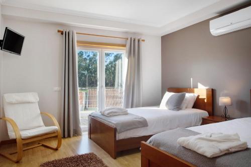 a bedroom with two beds and a chair and a window at Villa Rosa com Piscina e Jacuzzi in Salir de Matos