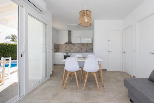 a white kitchen with a table and white chairs at Chalet a 150m de la playa y piscina privada in Cala en Bosc