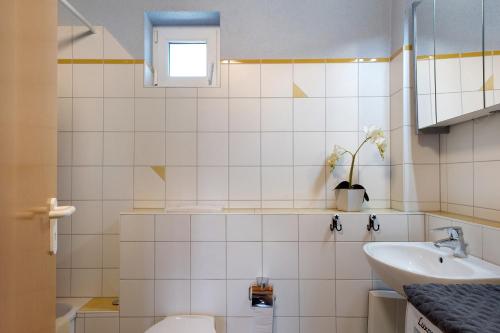a white tiled bathroom with a sink and a toilet at Ferienwohnung Lang, 45qm in Sasbach am Kaiserstuhl