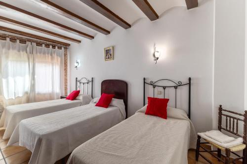 two beds in a room with white walls and red pillows at Casa Rural La Abubilla in Valdelaguna