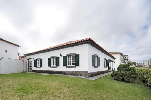 a white house with green shutters and a yard at Pascoal House in Ribeira Grande