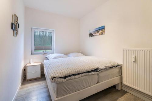 a white bedroom with a bed and a window at Ferienhaus Ostseeblick in Munkbrarup