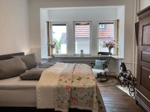 a bedroom with a bed and two windows and a chair at Ferienwohnung Luise in Münsingen