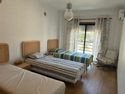 a bedroom with two beds and a chair and a window at Atlantic Lodge, 1ª linha de praia! in Costa da Caparica