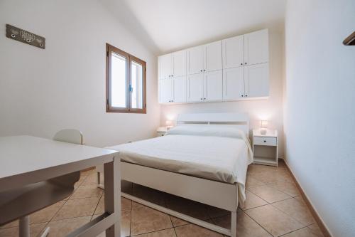 a white bedroom with a bed and a desk at Casa Perla in Villasimius