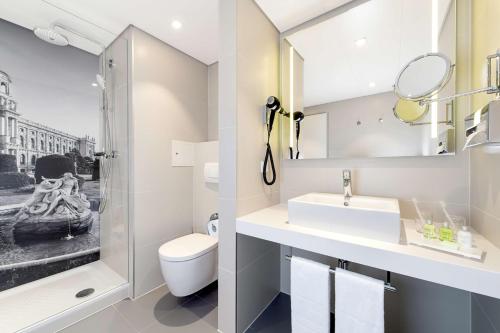 a bathroom with a sink and a toilet and a mirror at NH Collection Wien Zentrum in Vienna