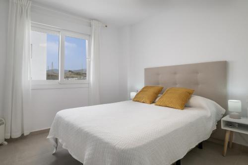 a white bedroom with a large bed with two yellow pillows at Moderno Apartamento Atlanterra in Zahara de los Atunes