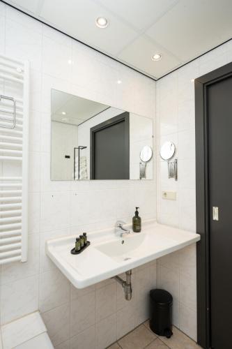 a white bathroom with a sink and a mirror at Hotel het Uilenbos in De Koog