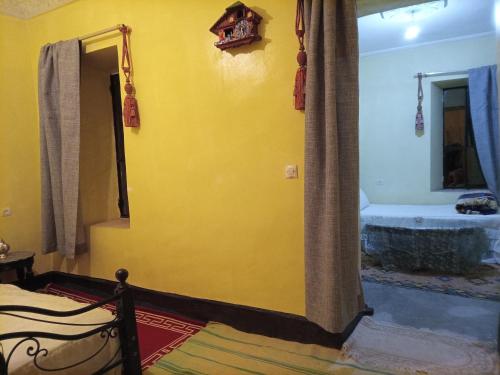 a bedroom with a yellow wall with a bed and a tub at Palmas Magramane Ogandou in Skoura