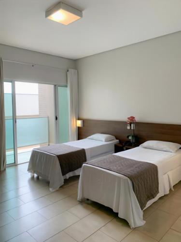 two beds in a room with a large window at Oásis Hotel in Araguaína