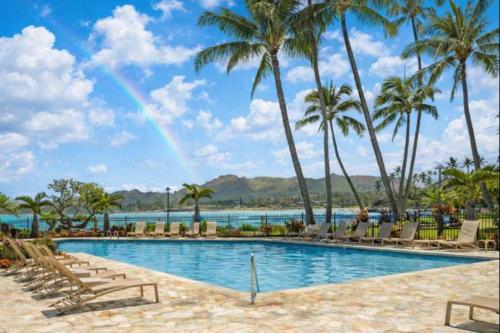 a pool with palm trees and a rainbow at NEW Beachfront 2 Bedroom Ocean View Oasis and Pool in Kapaa