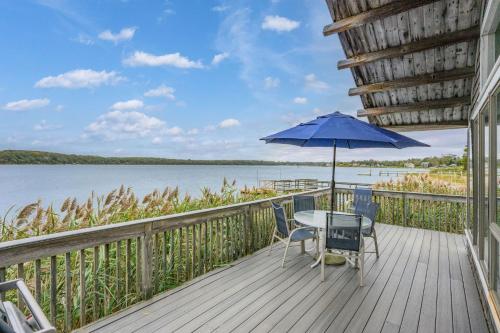 a table and chairs on a deck with a blue umbrella at Charming Waterfront Escape Along the Cove in Eastham
